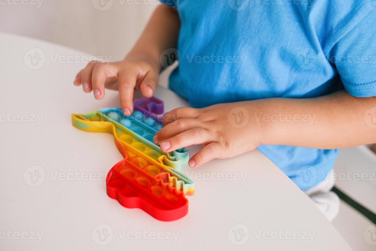 Little boy plays with rainbow Pop it fidget toy. Antistress children game. Children's trendy silicone toys pop it to relieve stress and develop hand motor skills. Colorful hand toy with push bubbles. photo