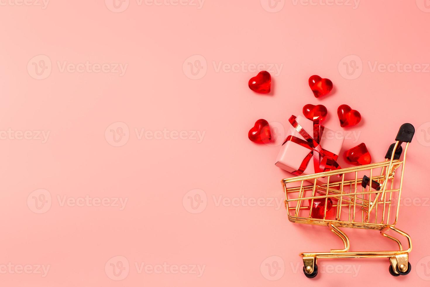 Shopping cart, trolley with little gift box and hearts on pink background with free space for text, copy space. Valentine's Day, sale. photo