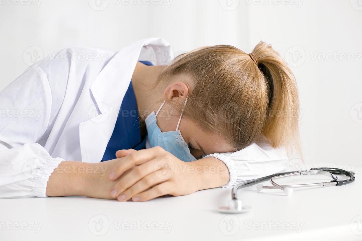 Tired and exhausted nurse or doctor. Stressed female medical worker with protective face mask, depressed after working over hours due to coronavirus outbreak. Covid 19. Medicine, healthcare, pandemic photo