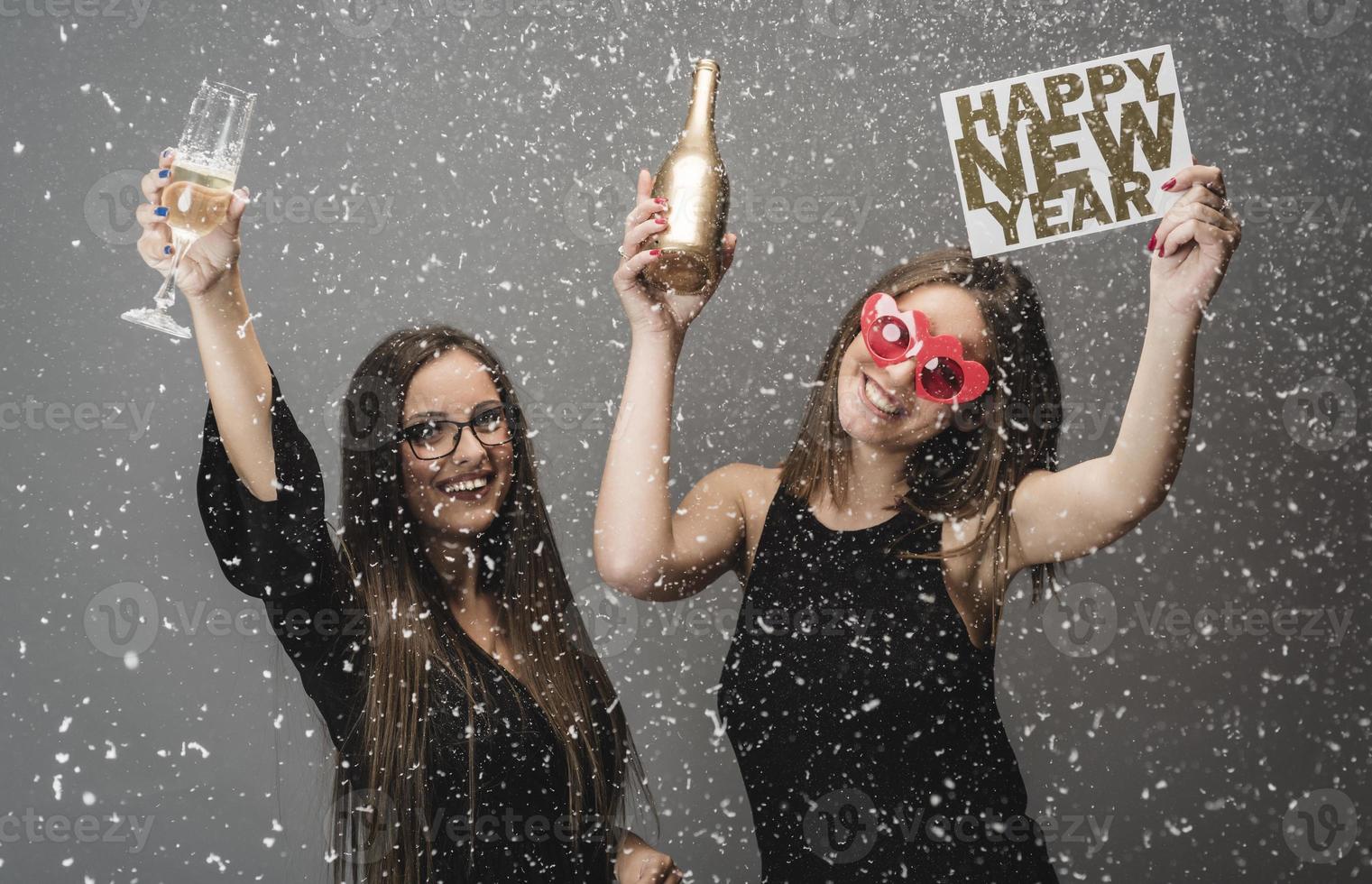 Two female friends celebrating New Year with confetti and champagne holding sign. isolated photo