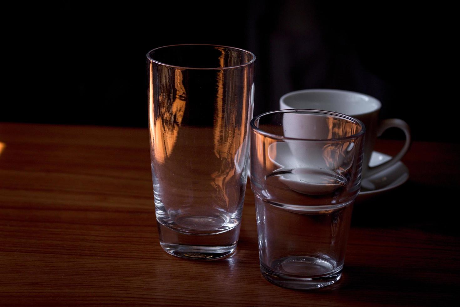 Transparent glass water glasses and coffee mugs placed on a wooden table. photo
