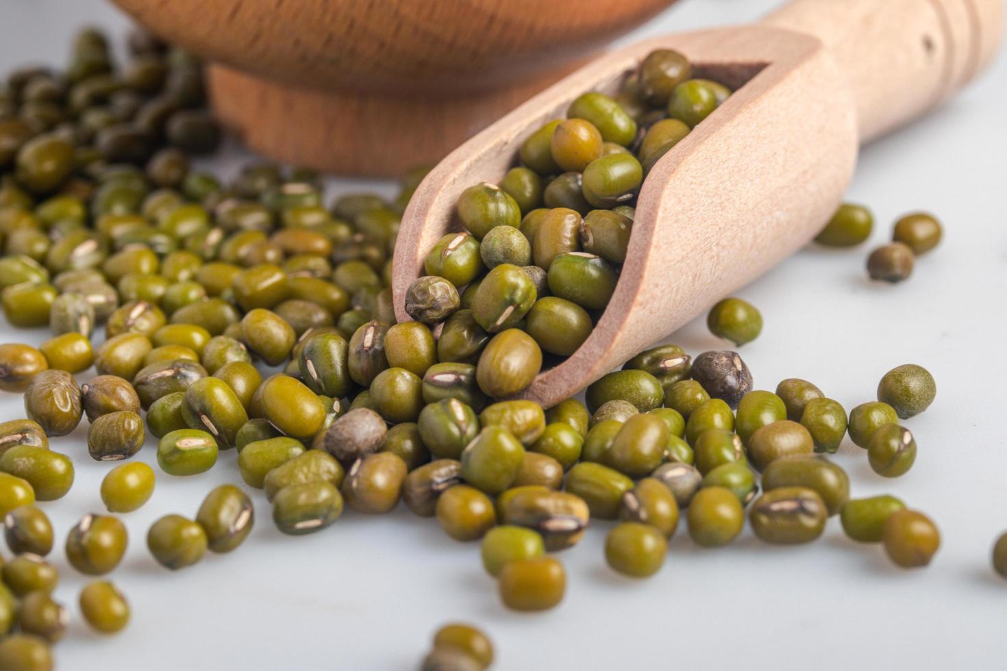 Raw green peas in wooden spoon on white background photo