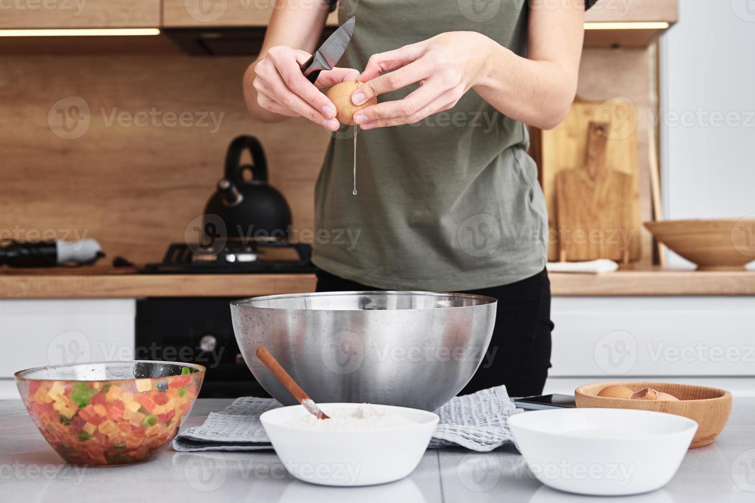 Woman in kitchen cooking a dough. Hands breaks an egg into a bowl photo