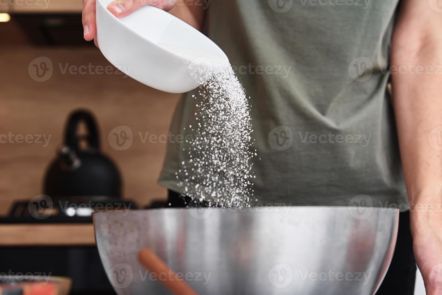 Woman in kitchen cooking a dough. Hands pour flour into a bowl photo