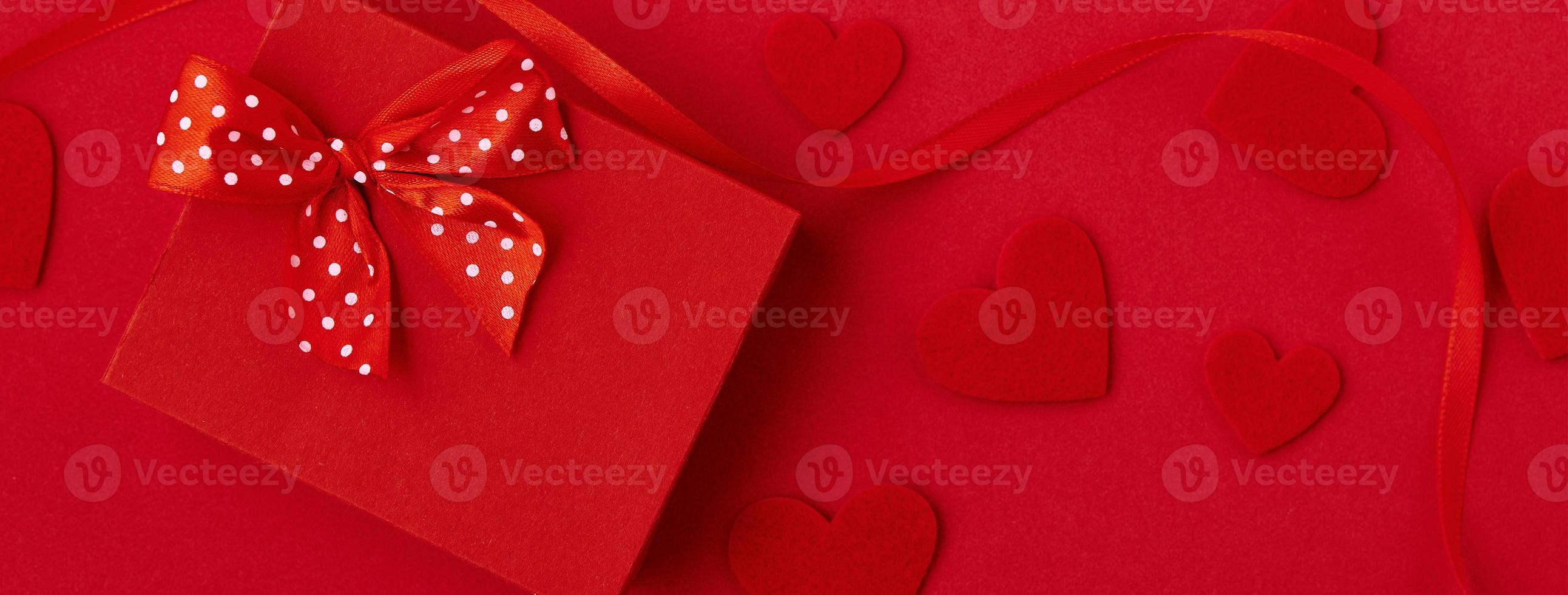 Gift box with festive ribbon and hearts on the red background photo
