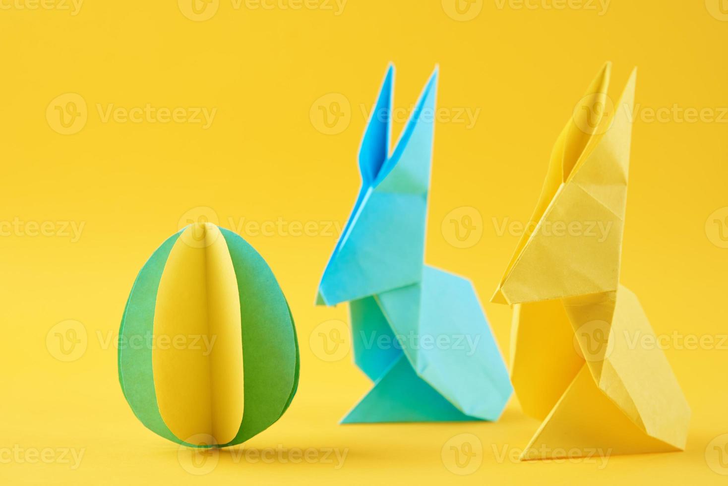 dos conejos de origami de papel y huevo de color sobre fondo amarillo foto