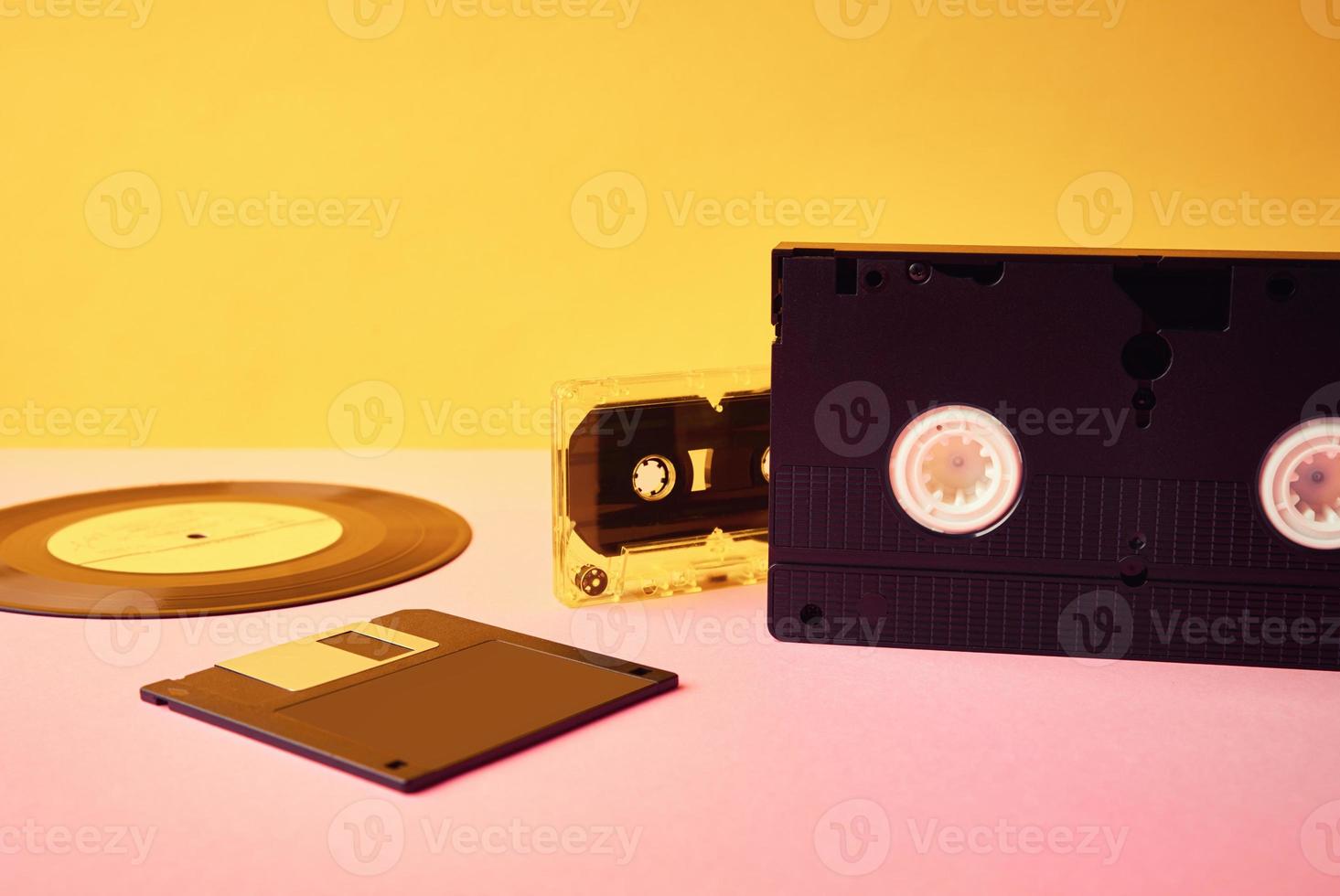 Vinyl disc, floppy diskette, vhs and tape cassete on yellow background photo