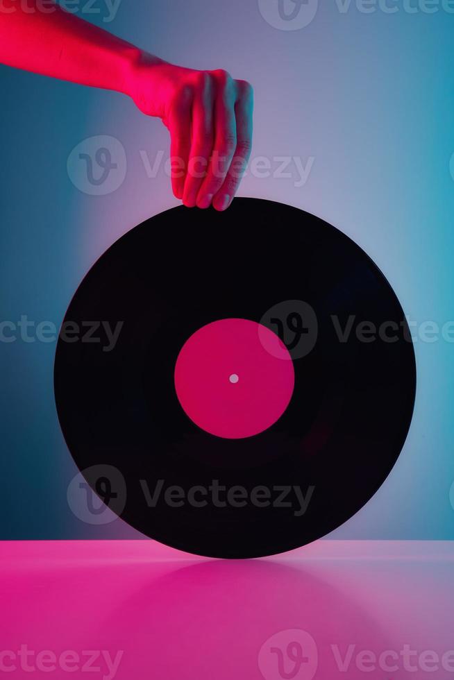 Hand hold retro vinyl disc with neon lights. Vintage music background photo