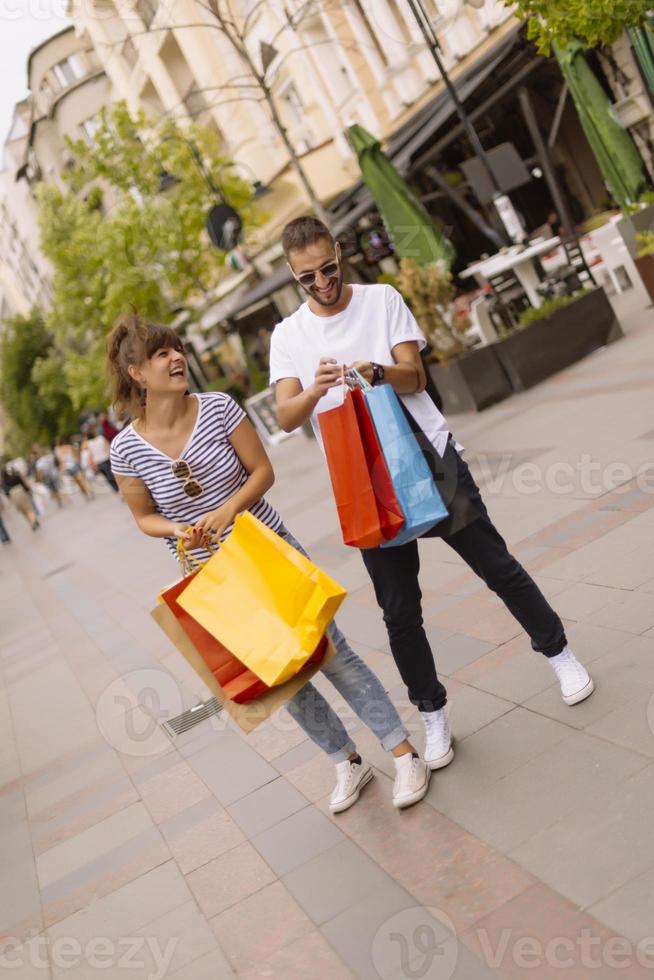 retrato de una alegre pareja joven caucásica hombre y mujer sosteniendo muchas bolsas de papel después de ir de compras mientras camina y habla en la calle. feliz pareja familiar con paquetes al aire libre. concepto de compra foto