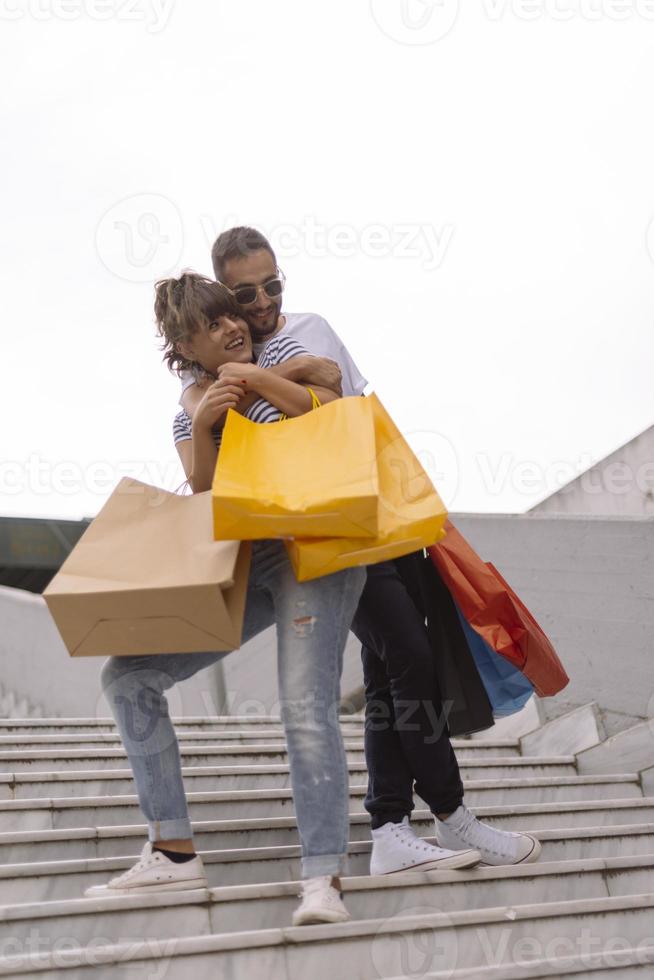 retrato de una alegre pareja joven caucásica hombre y mujer sosteniendo muchas bolsas de papel después de ir de compras mientras camina y habla en la calle. feliz pareja familiar con paquetes al aire libre. concepto de compra foto