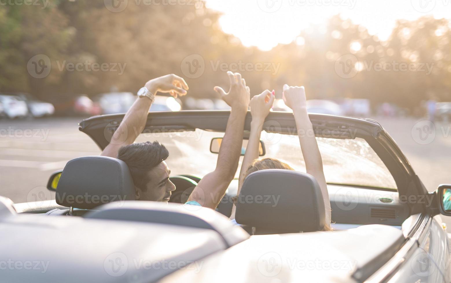 Friends having fun at car trip around the world. Couple in love with arms up on a convertible car. photo