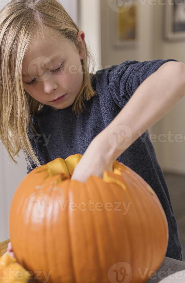 hermoso niño rubio tallando calabaza con cuchillo para halloween. concepto de halloween foto