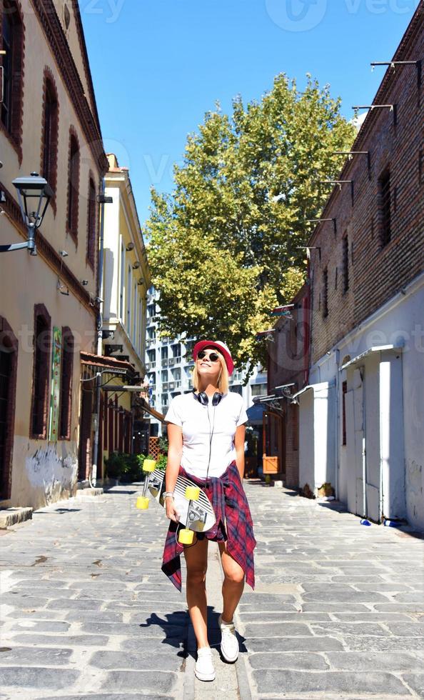 Beautiful hipster girl with skate board wearing sunglasses in the city. photo