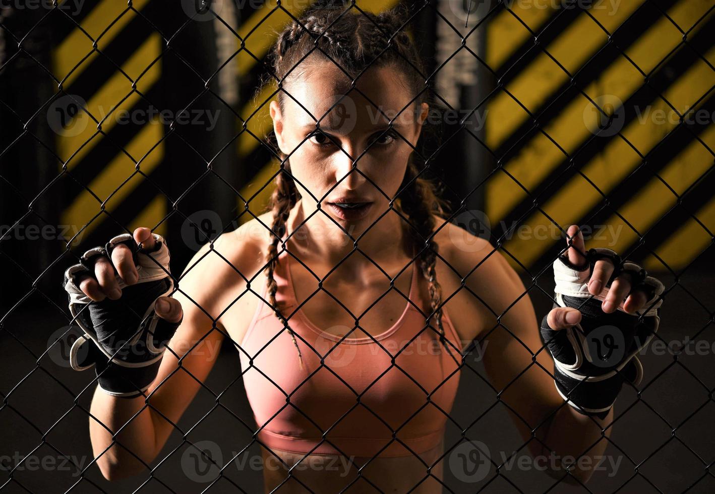 A female trainee of mixed martial arts wearing a hand wrap warms up within the ring cage by stretching her back and legs. photo