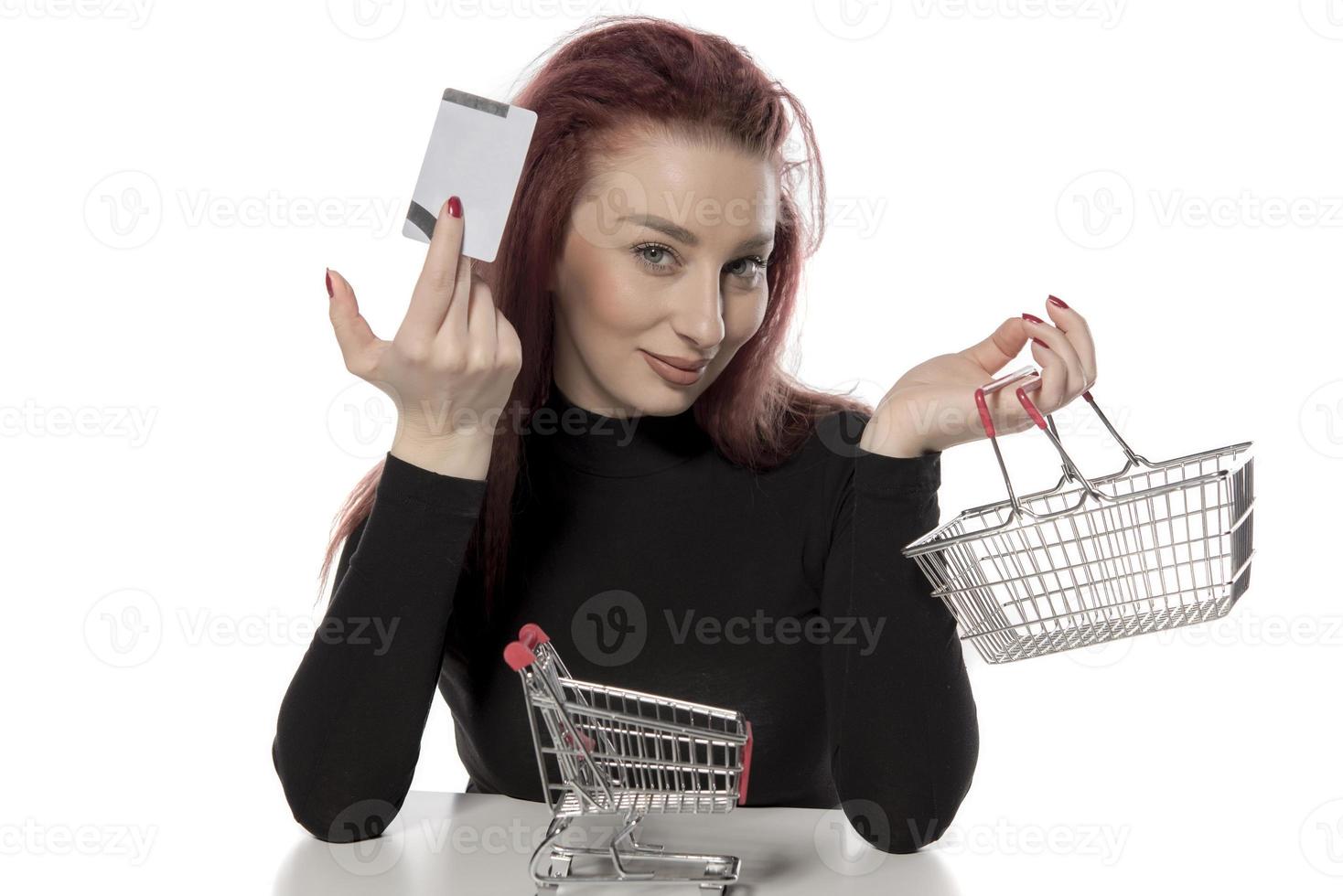 Happy female holding credit cards and a small empty shopping cart isolated on white background photo