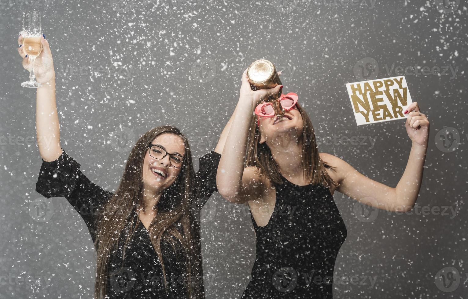 Two female friends celebrating New Year with confetti and champagne holding sign. isolated photo