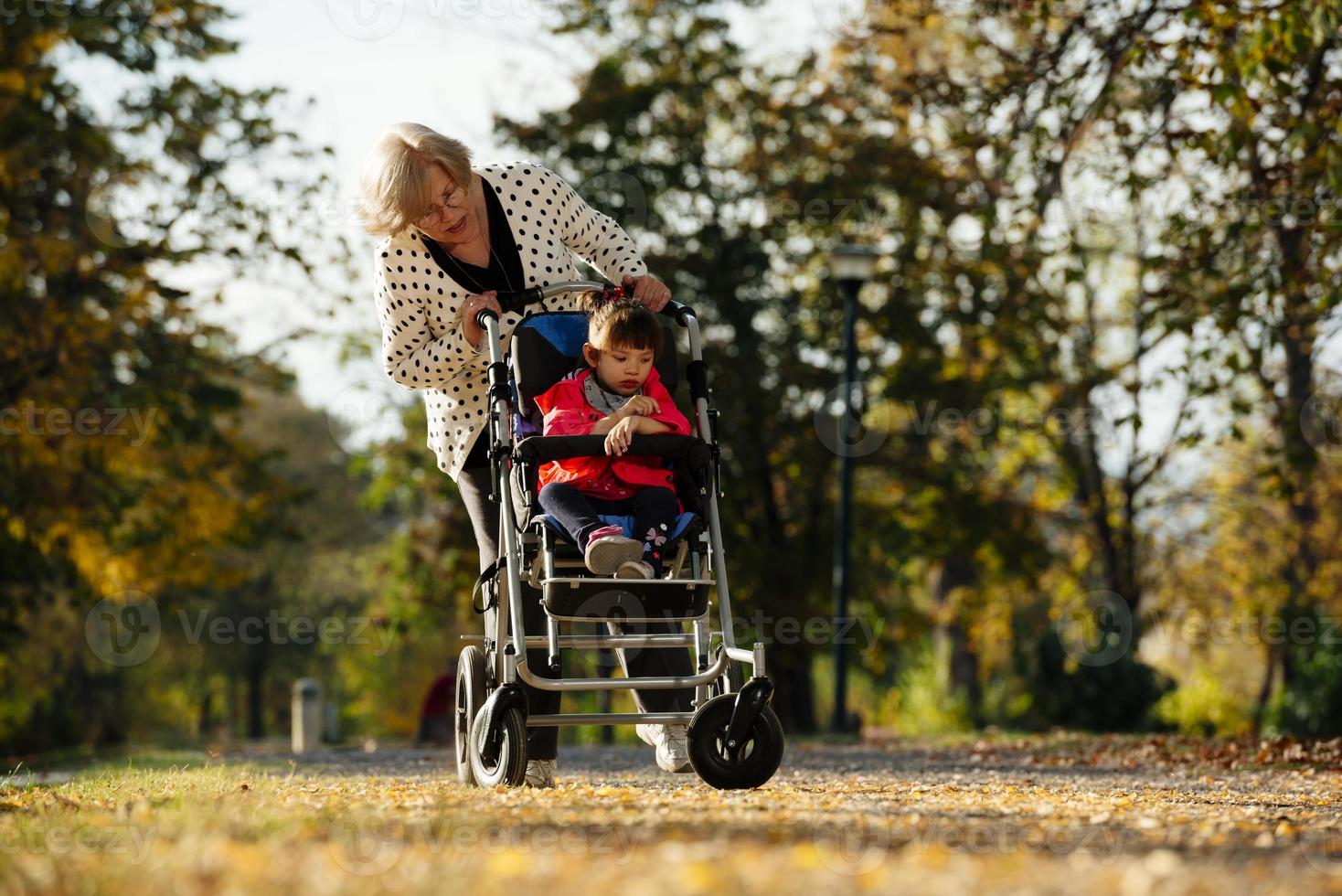 Grandmother and her autistic grand daughter enjoying holiday together outdoors, lying on green grass on blanket and smiling to camera. Leisure family lifestyle, happiness and moments. photo