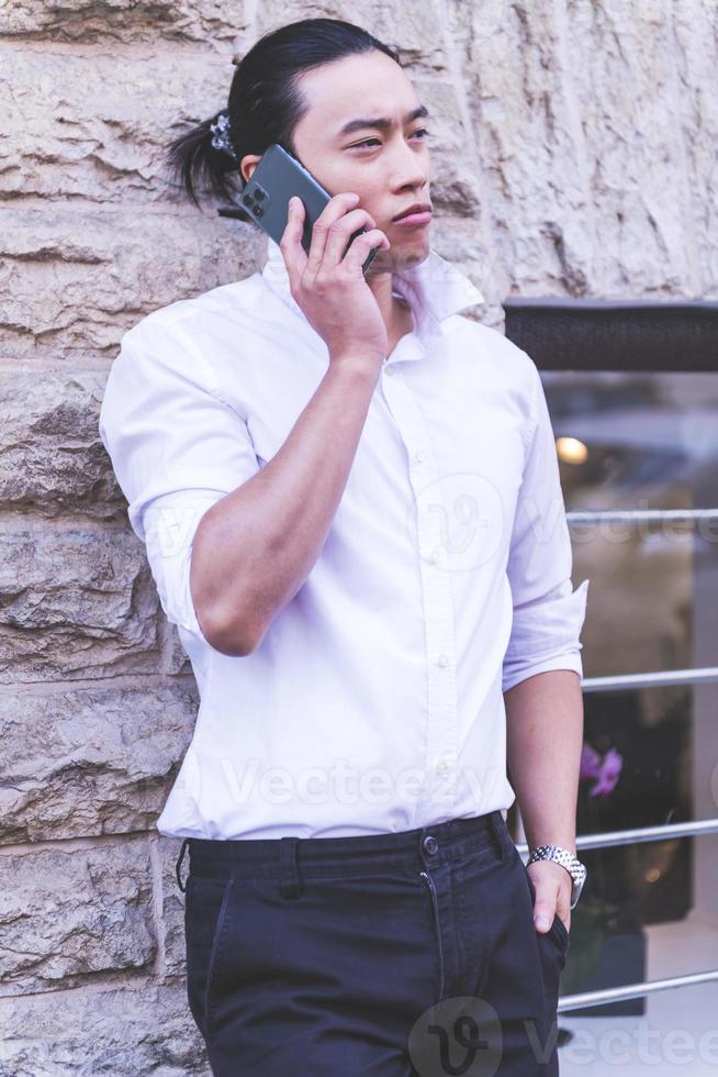 portrait of Young smiling handsome Asian man in semi formal suit using mobile phone photo