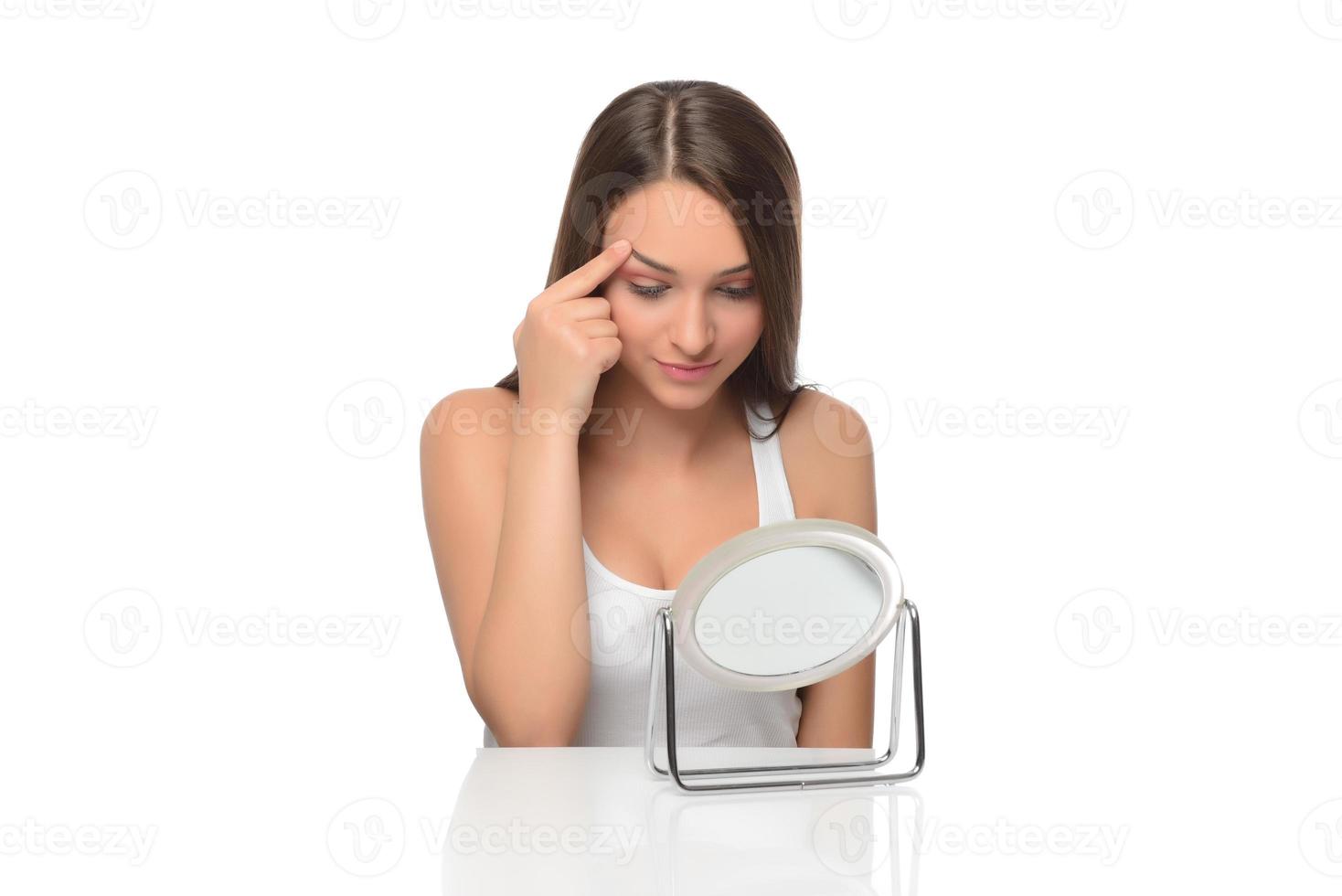 Acne prone skin concept. Young woman looking at mirror at home, checking her face skin photo