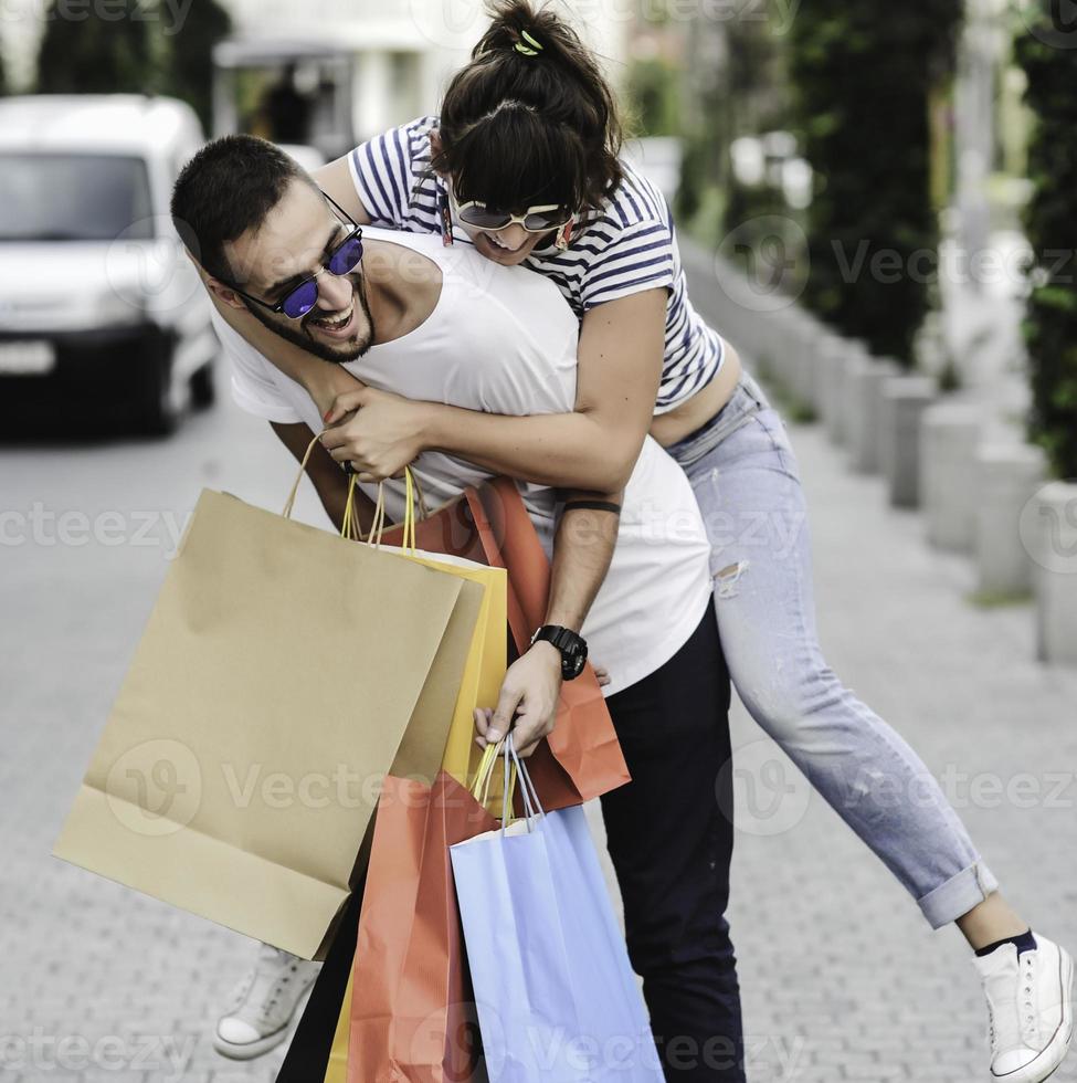 retrato de una alegre pareja joven caucásica hombre y mujer sosteniendo muchas bolsas de papel después de ir de compras mientras camina y habla en la calle. feliz pareja familiar con paquetes al aire libre. concepto de compra foto