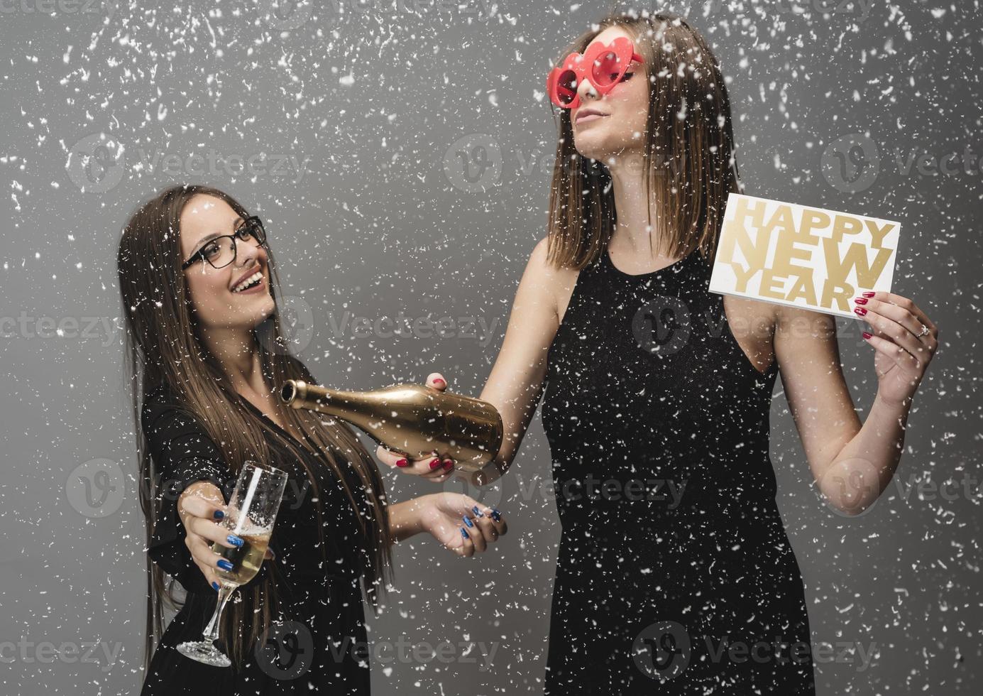 Two female friends celebrating New Year with confetti and champagne holding sign. isolated photo