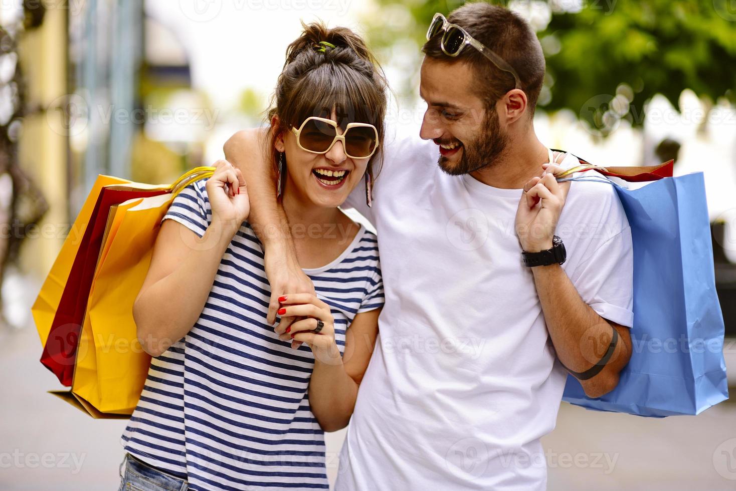 Portrait of cheerful Caucasian young couple man and woman holding many paper bags after shopping while walking and talking on street. Happy family couple with packages outdoor. Buying concept photo