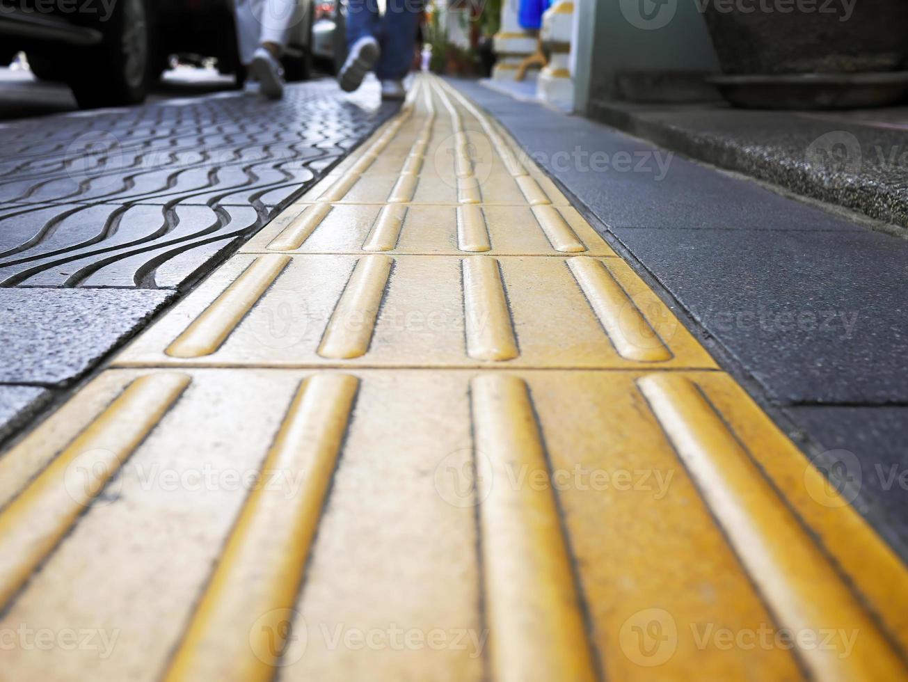 vista en perspectiva de ángulo bajo de peatones caminando con pavimentación táctil de guía ciega amarilla para discapacidad, y personas ciegas, textura en baldosas para discapacidad, enfoque selectivo, sendero foto