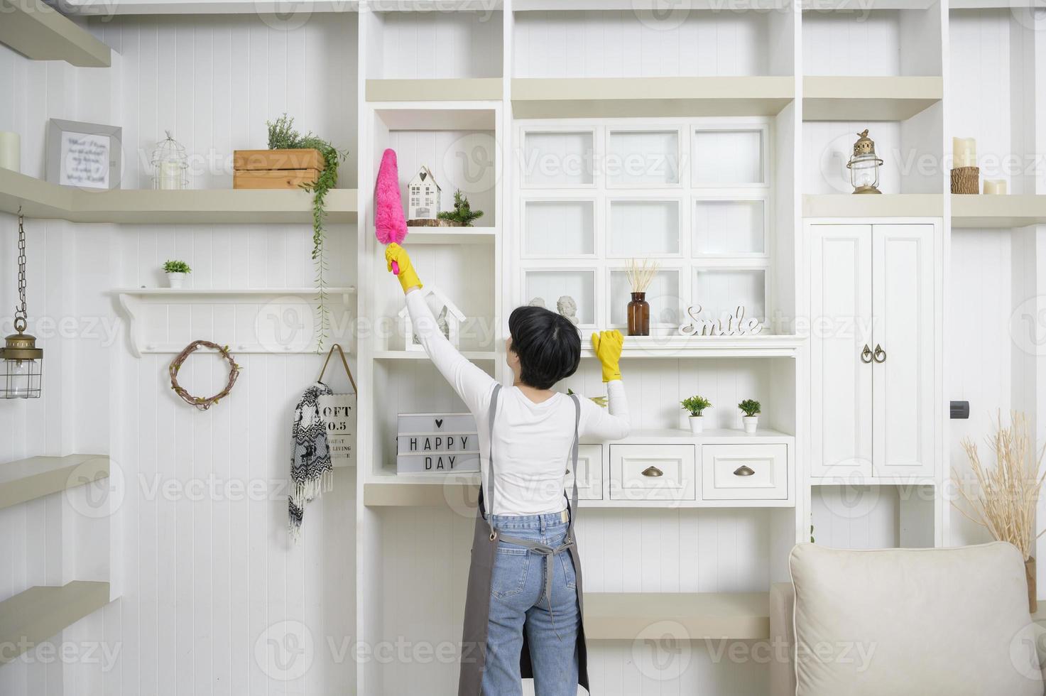 Happy Asian young woman sweeping sofa and furniture to cleaning house, healthy lifestyle concept photo