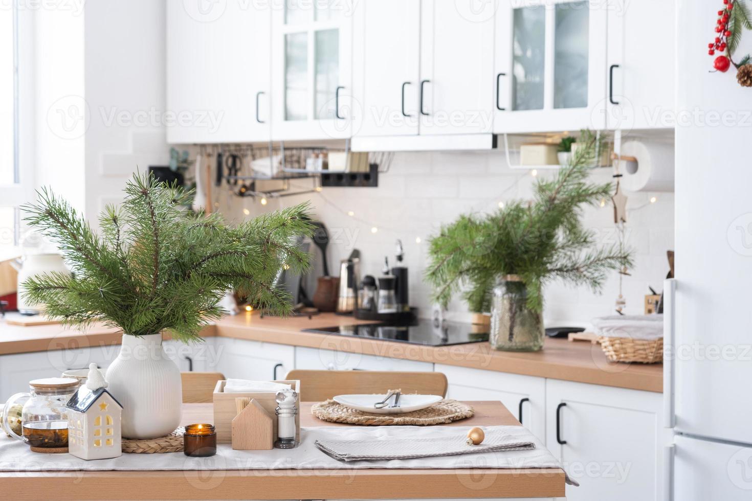 decoración navideña festiva en cocina blanca, desayuno festivo, interior escandinavo blanco. la figura de una casa acogedora en la mesa puesta. año nuevo, estado de ánimo, hogar acogedor. copie el espacio foto