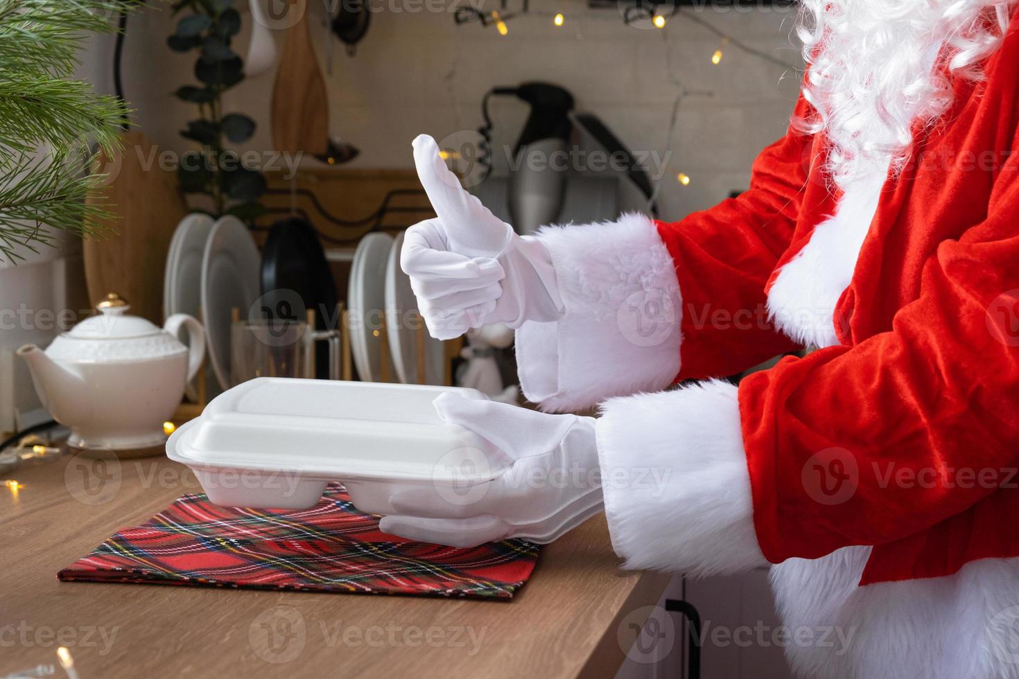 Food delivery to home service containers in hands of Santa Claus puts it on kitchen table and takes it away, thumbs up. Ready-made hot order, Christmas, New year holidays catering. photo