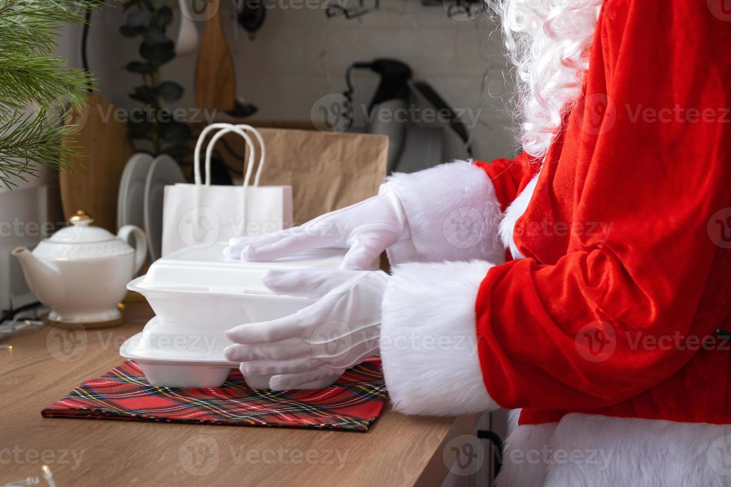 Food delivery to home service containers in hands of Santa Claus puts it on kitchen table and takes it away. Ready-made hot order, Christmas, New year holidays catering. photo