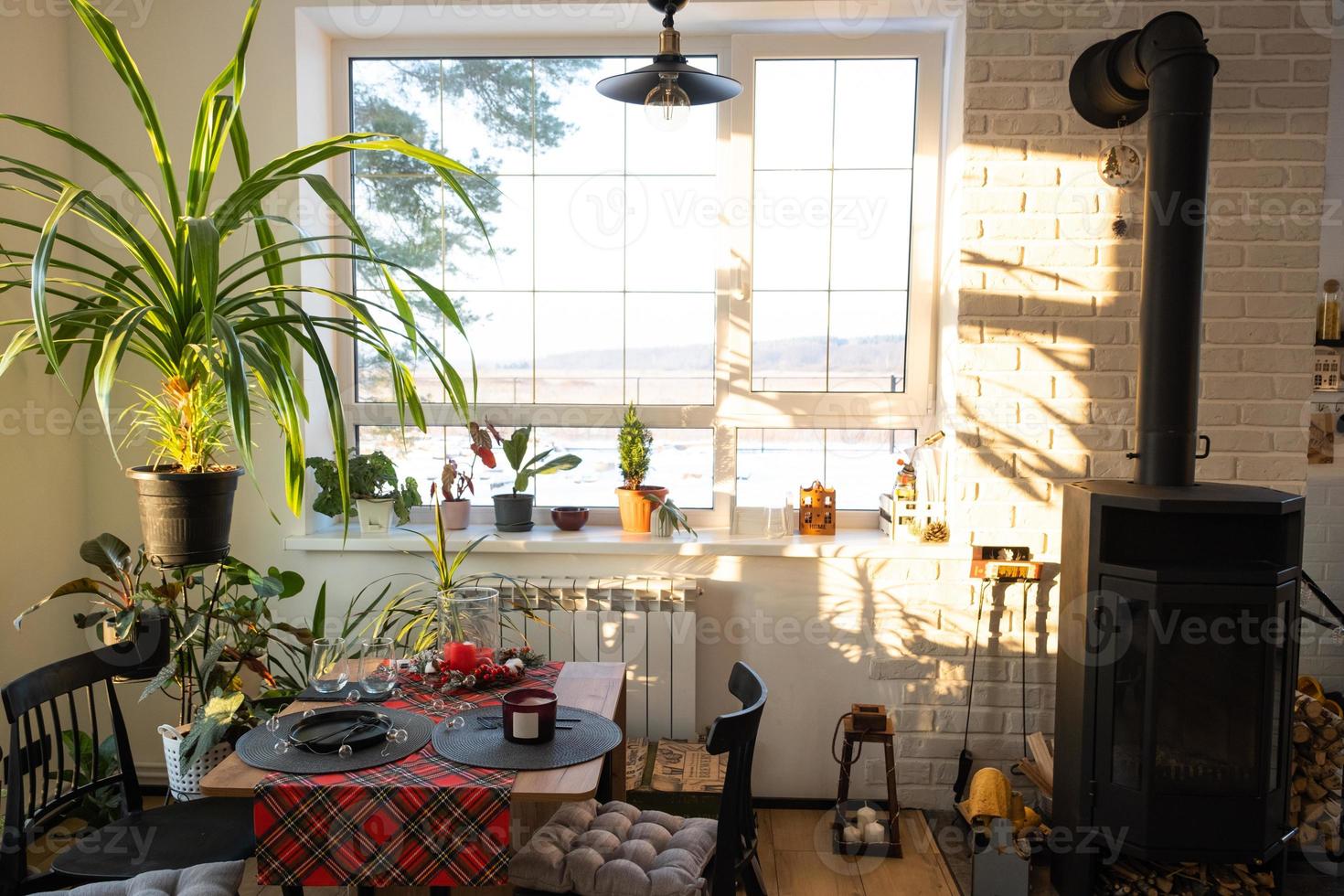 Sunny interior of a loft-style house with potted plants, a large window, a covered table for the Christmas and New Year holidays photo