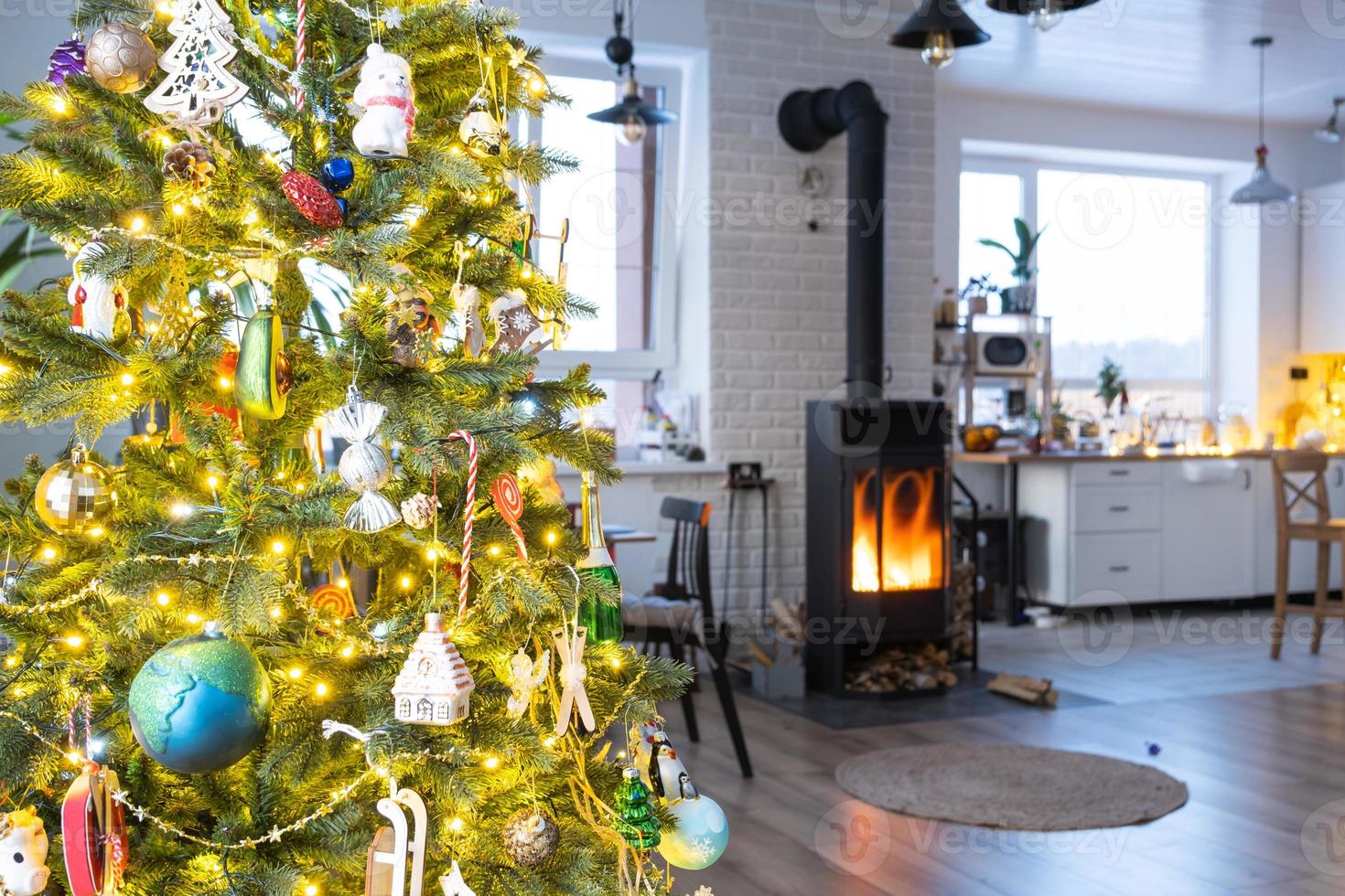 Festive interior of house is decorated for Christmas and New Year in loft style with black stove, fireplace, Christmas tree. Warm studio room with set table, burning wood, cozy and heating of home photo