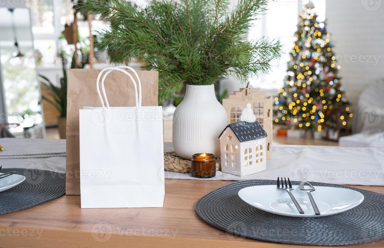 los paquetes de papel se burlan en la mesa servida en la cocina decorada para navidad. compras y regalos, presentes y comidas preparadas se entregan y preparan para el nuevo año foto