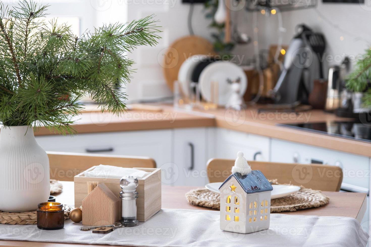 decoración navideña festiva en cocina blanca, desayuno festivo, interior escandinavo blanco. la figura de una casa acogedora en la mesa puesta. año nuevo, estado de ánimo, hogar acogedor. copie el espacio foto