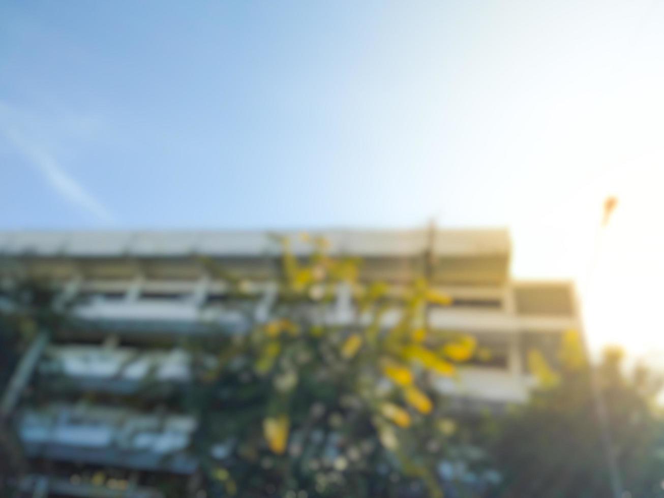 Blurred image of white buildings, blue sky, green trees with yellow flowers in the morning. photo