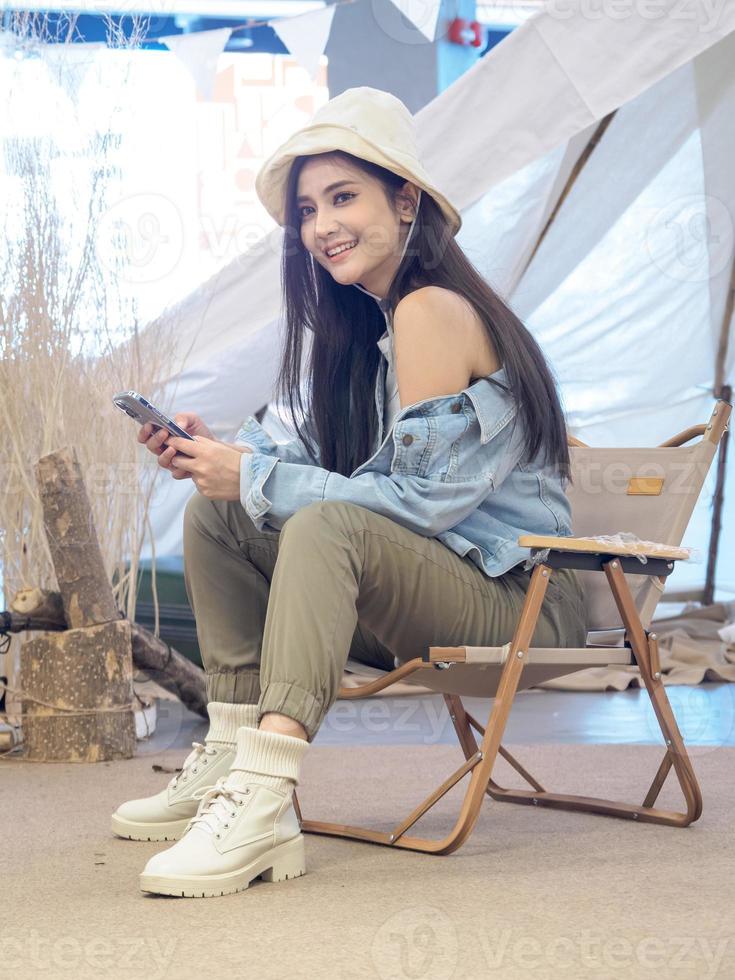 Portrait beautiful young girl woman Asian pretty smile one person alone sitting on chair camping with using tablet connected the Internet to work. travel trip in front tent freedom relax happy enjoy photo