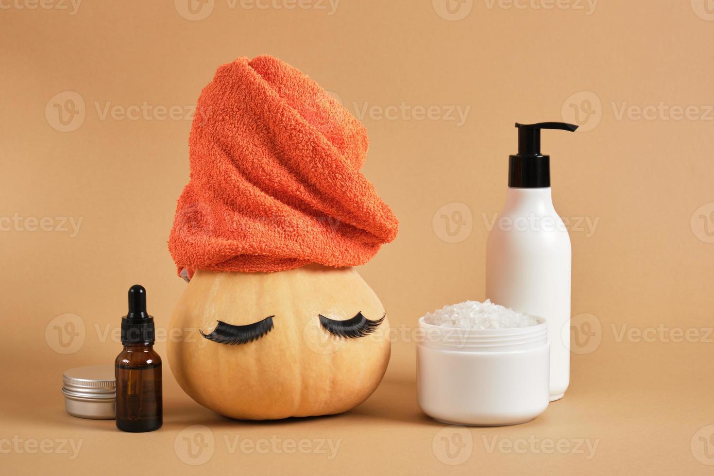 mock up set of cosmetic containers and pumpkin with towel and false eyelashes on beige background photo