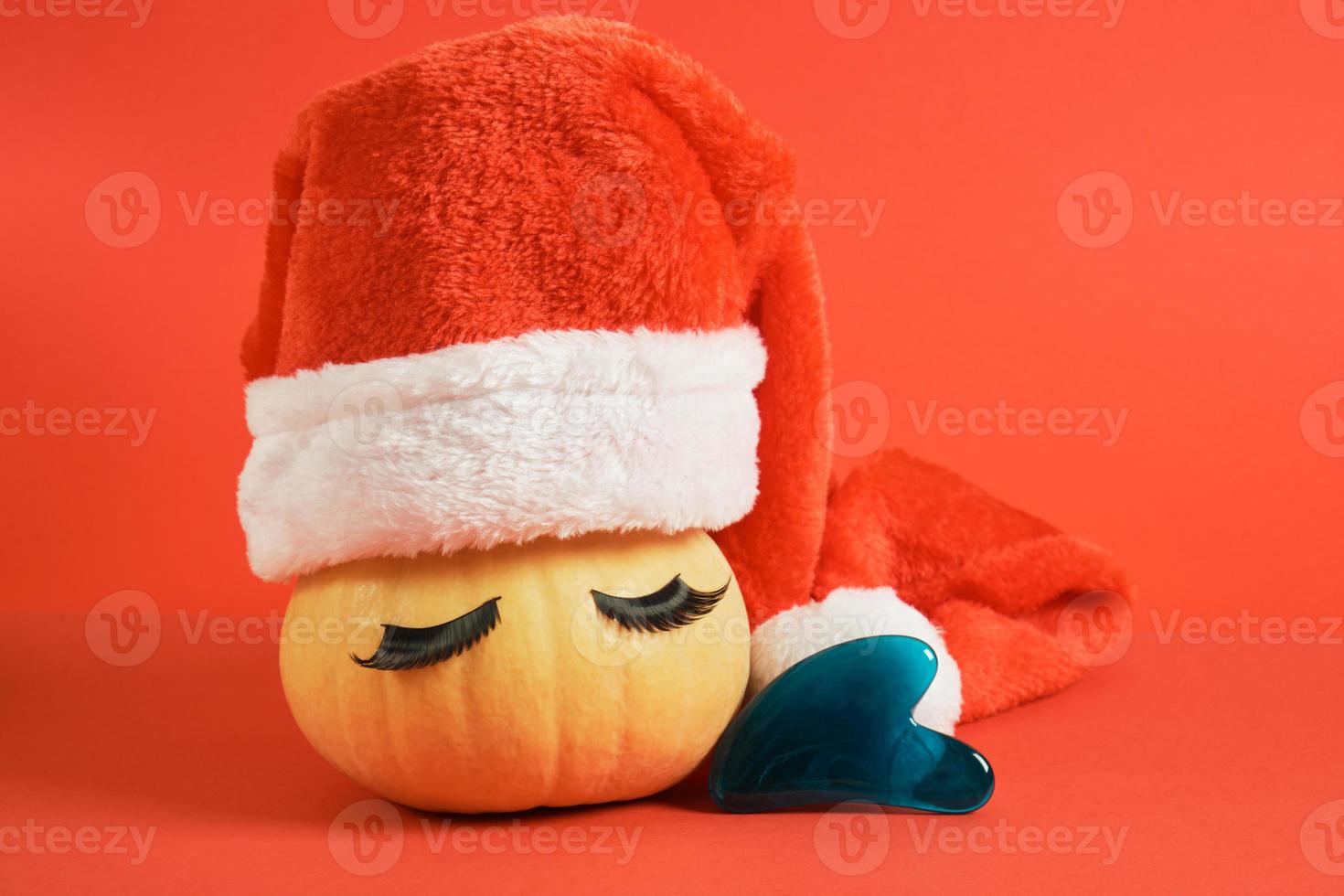 scraper gau sha made of plastic and cute pumpkin with false eyelashes and santa hat on a red background photo