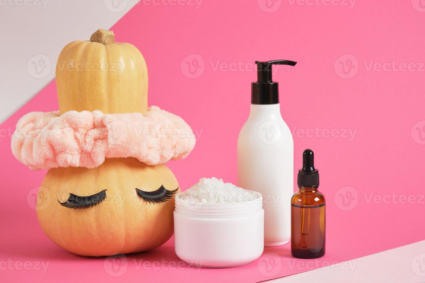 mock up set of cosmetic containers and pumpkin with headband and false eyelashes on pink background photo