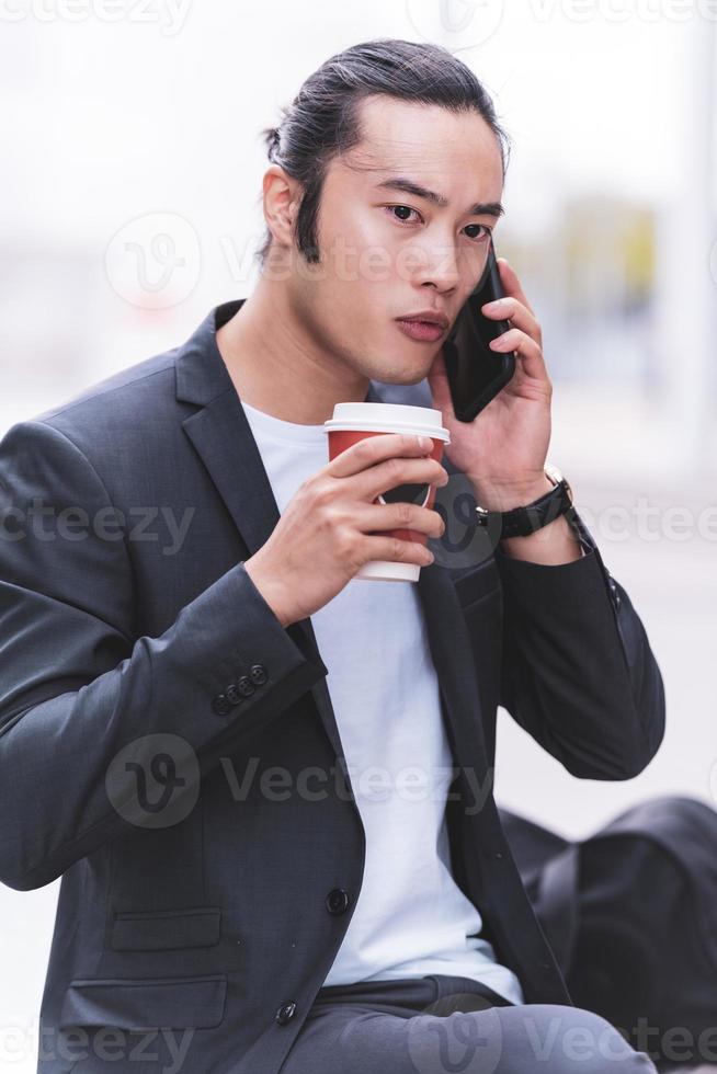 portrait of Young smiling handsome Asian man in semi formal suit using mobile phone photo