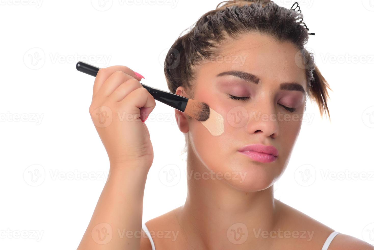 Portrait of a young woman applying make up on her face. Isolated on white background photo