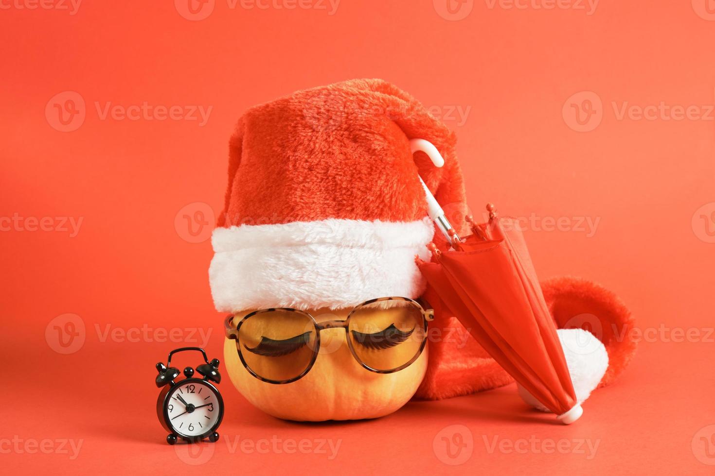 calabaza con gafas de sol y gorro de Papá Noel bajo un concepto de vacaciones de paraguas en países cálidos foto