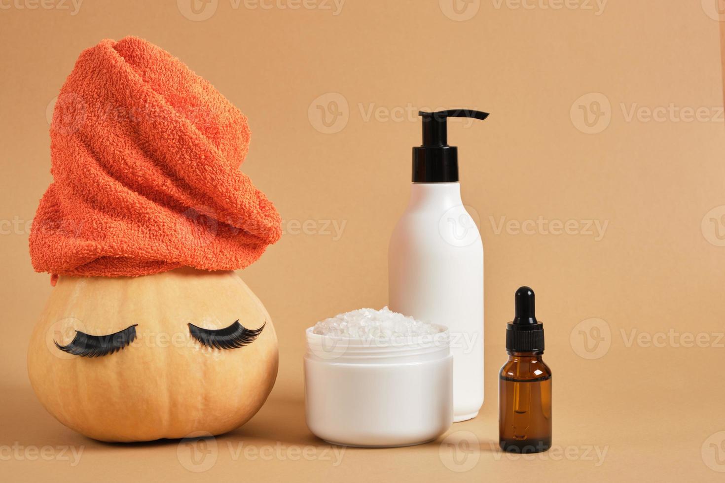 mock up set of cosmetic containers and pumpkin with towel and false eyelashes on beige background photo