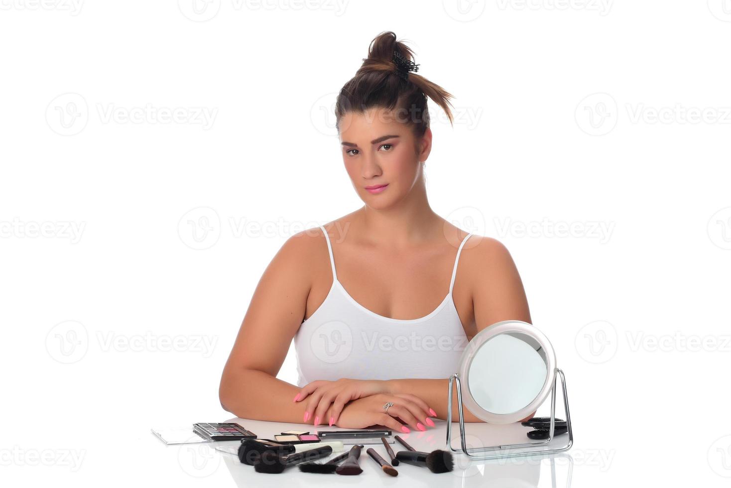 beautiful attractive brunette woman checking her face skin in front of a mirror on white background. photo