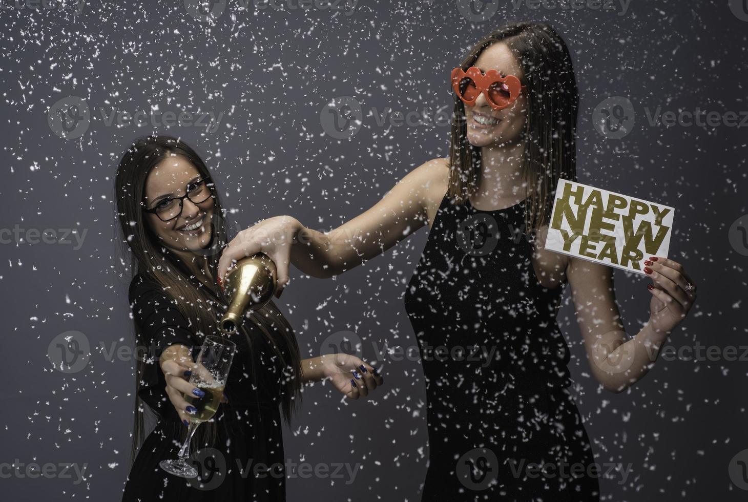 Two female friends celebrating New Year with confetti and champagne holding sign. isolated photo