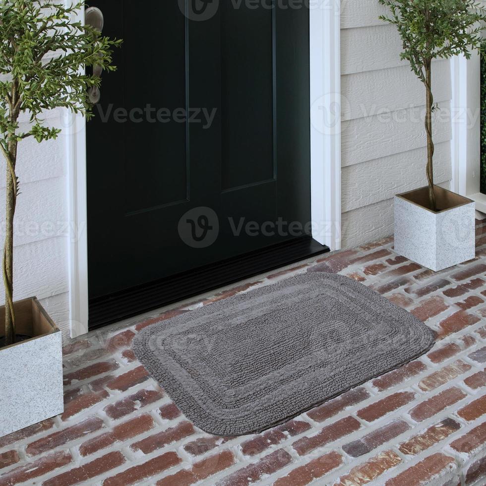 felpudo de entrada de bienvenida de diseñador colocado en un piso de ladrillo macizo fuera de la puerta de entrada con plantas foto