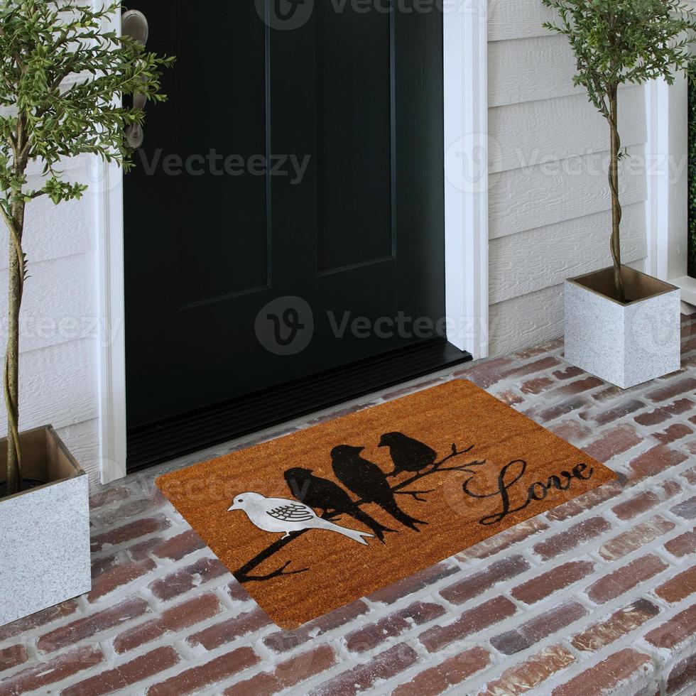 Designer Welcome Entry Doormat Placed on Solid Brick Floor Outside Entry Door with Plants photo