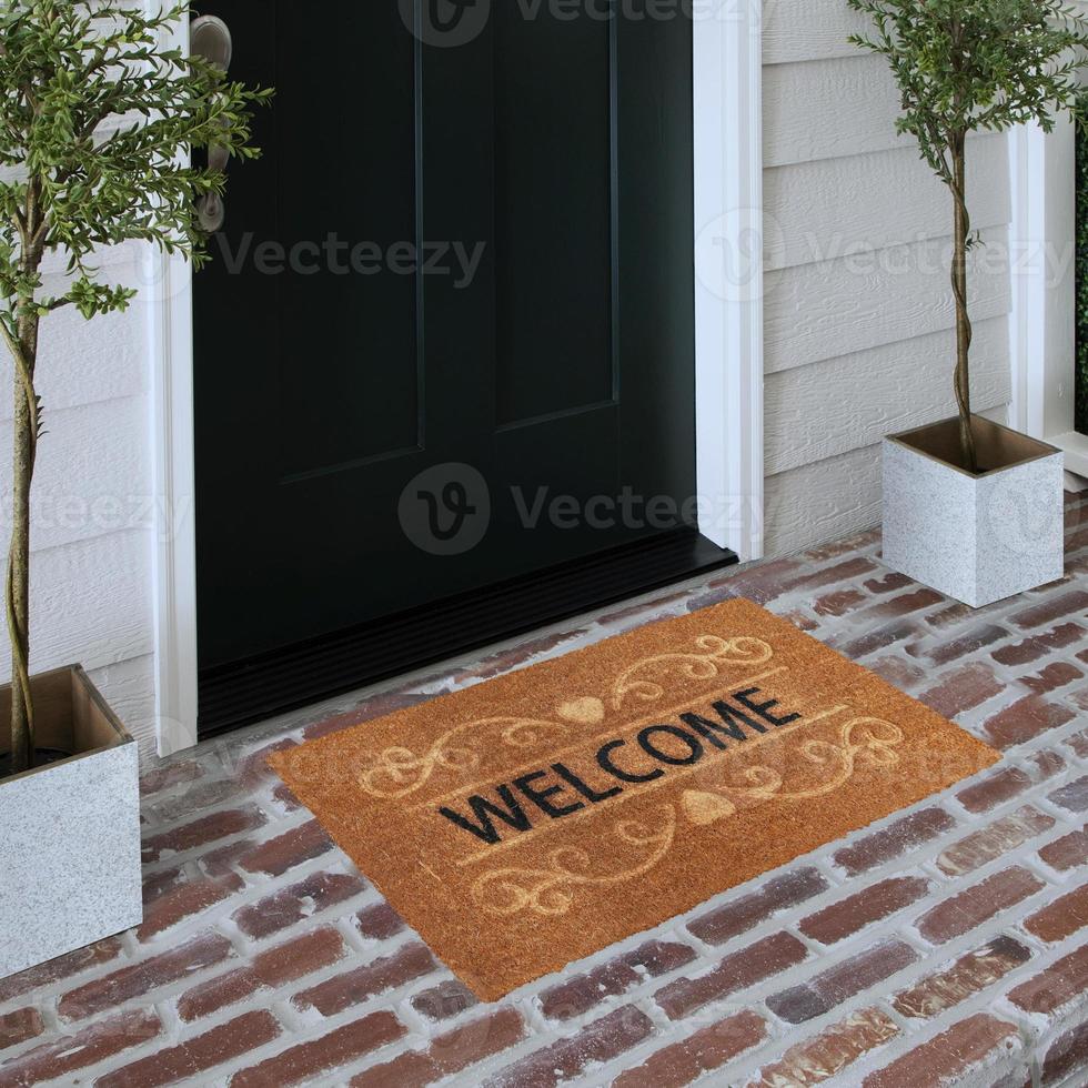 Designer Welcome Entry Doormat Placed on Solid Brick Floor Outside Entry Door with Plants photo