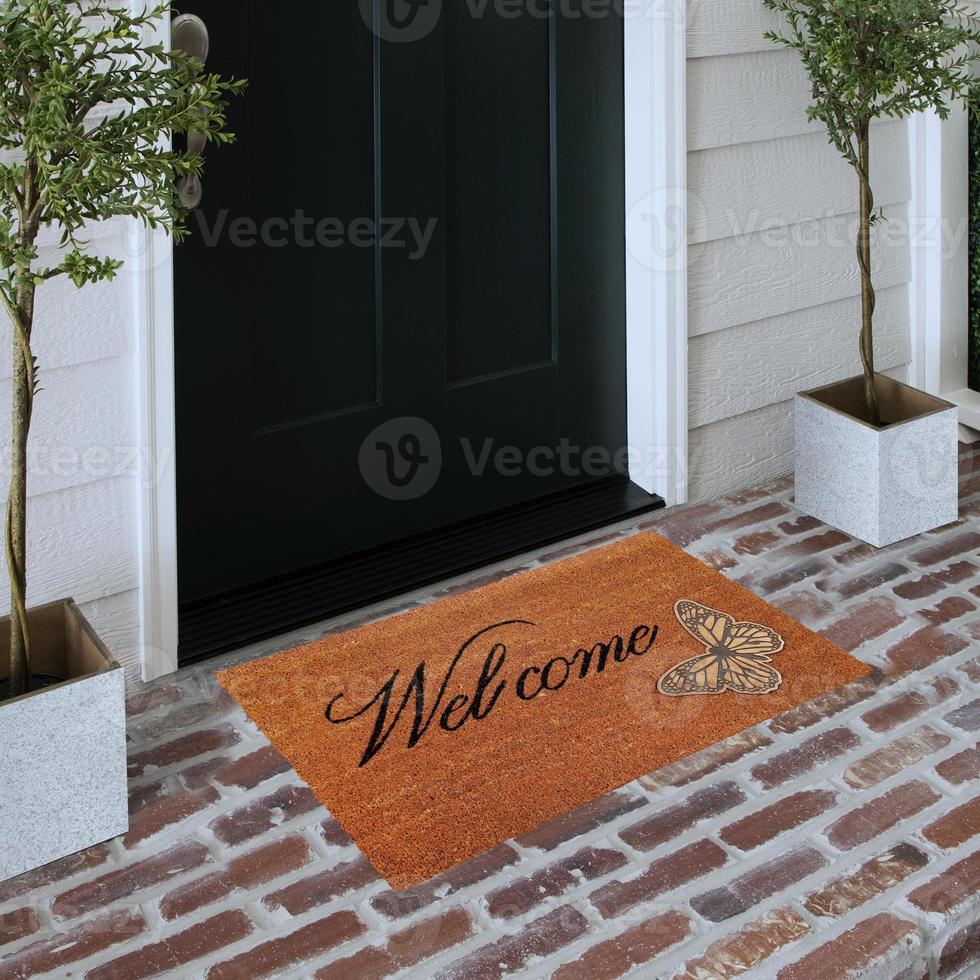 Designer Welcome Entry Doormat Placed on Solid Brick Floor Outside Entry Door with Plants photo